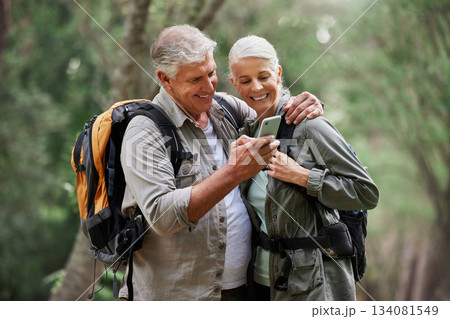 Phone, video call and elderly couple hiking in a forest, happy and smile while bonding on adventure. Active seniors, online and maps for man and woman backpacking in nature while checking location 134081549