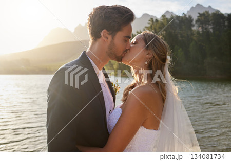 Love, wedding and a newlywed couple kissing by a lake outdoor in celebration of their marriage for romance. Water, summer or kiss with a bride and groom bonding together in tradition after ceremony Love, wedding and a newlywed couple kissing by a lake outdoor in celebration of their marriage for romance. Water, summer or kiss with a bride and groom bonding together in tradition after ceremony 134081734