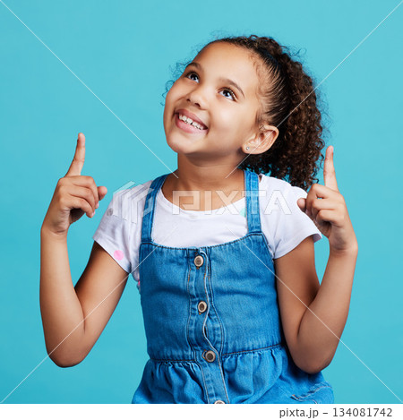 Happy, looking and a child pointing in a direction isolated on a blue background in a studio. Smile, thinking and a young girl showing up with a hand gesture, advertising and counting on a backdrop Happy, looking and a child pointing in a direction isolated on a blue background in a studio. Smile, thinking and a young girl showing up with a hand gesture, advertising and counting on a backdrop 134081742