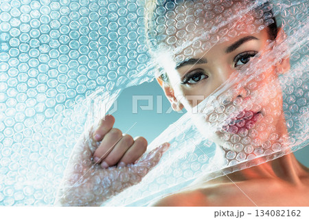 Bubble wrap, beauty and portrait of woman with makeup, cosmetics and skincare products in studio. Creative art, salon aesthetic and girl with face glow, lipstick and luxury style with plastic tear 134082162