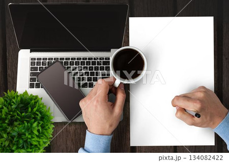 Man writing on paper while drinking coffee Man writing on paper while drinking coffee 134082422