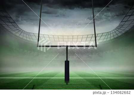American football goal post is standing on green striped turf in misty stadium under overcast sky 134082682