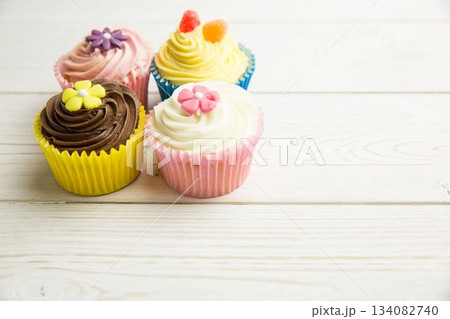 Four decorated cupcakes are sitting on pale wood tabletop in flat design with sugar flower toppings Four decorated cupcakes are sitting on pale wood tabletop in flat design with sugar flower toppings 134082740