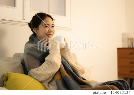 夜の灯りの部屋でホットドリンクを飲む若い女性　女性の冬イメージ　白熱灯のあたたかいイメージ 134083124