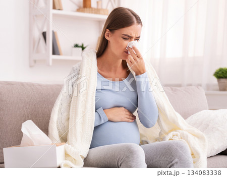 Pregnancy And Flu. Sick Expectant Girl Blowing Nose In Tissue Sitting On Sofa At Home 134083338