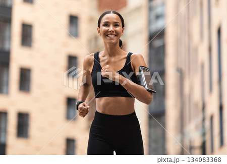 Healthy Lifestyle Concept. Sporty Young Arabic Female Jogging On Urban City Street, Athletic Woman In Stylish Sportwear And Phone Holder Armband Training Outdoors, Enjoying Running, Copy Space 134083368