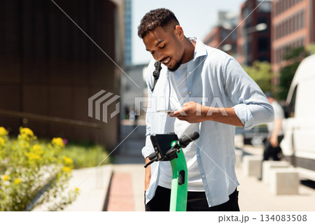 Electric push scooter sharing services. Young black guy renting motorized kick e-scooters in the city, paying online with smartphone. Urban lifestyle 134083508