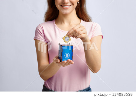 Garbage Sorting Conceptual Image With Woman Putting Card With Paper Waste Icon Into Small Wooden Toy Trash Container, Unrecognizable Lady Standing Over Light Background In Studio, Copy Space Garbage Sorting Conceptual Image With Woman Putting Card With Paper Waste Icon Into Small Wooden Toy Trash Container, Unrecognizable Lady Standing Over Light Background In Studio, Copy Space 134083559