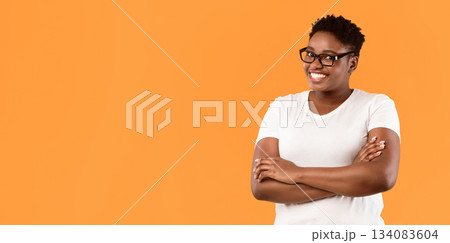 Happy Overweight African American Woman Standing Crossing Hands Posing Over Yellow Studio Background, Wearing White T-Shirt And Eyeglasses. Panorama With Empty Space For Text Happy Overweight African American Woman Standing Crossing Hands Posing Over Yellow Studio Background, Wearing White T-Shirt And Eyeglasses. Panorama With Empty Space For Text 134083604