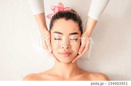 Young asian woman enjoying skin lifting face massage, getting professional beauty treatments at wellness center, attractive female relaxing on massage table with closed eyes, top view with copy space Young asian woman enjoying skin lifting face massage, getting professional beauty treatments at wellness center, attractive female relaxing on massage table with closed eyes, top view with copy space 134083951