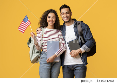 Study Abroad. Smiling Middle Eastern Students Couple Posing With American Flag In Hand, Happy Young Arab Man And Woman With Backpacks And Workbooks Standing Over Yellow Studio Background, Copy Space Study Abroad. Smiling Middle Eastern Students Couple Posing With American Flag In Hand, Happy Young Arab Man And Woman With Backpacks And Workbooks Standing Over Yellow Studio Background, Copy Space 134084208