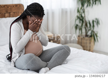 Sad Black Pregnant Woman Crying At Home, Having Maternity Depression, Suffering Hormonal Changes During Pregnancy, Desperate Lady Sitting On Bed In White Bedroom Covering Face With Hands, Copy Space 134084217