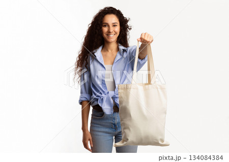 Happy Millennial Woman Showing White Eco Shopper Bag To Camera Posing Standing Over White Studio Background. Eco-Friendly Lifestyle, Minimalism Ecology Protection Concept 134084384