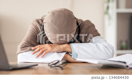 Overworked female doctor woman in hijab having nap at workdesk, working with laptop in clinic. Exhausted physician young lady leaning on her hands, needs for break during long working day Overworked female doctor woman in hijab having nap at workdesk, working with laptop in clinic. Exhausted physician young lady leaning on her hands, needs for break during long working day 134084430