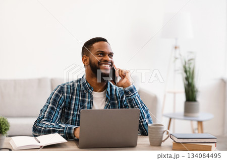 Smiling Black Businessman Talking On Phone Sitting At Workplace In Modern Office. Mobile Business Communication And Entrepreneurship. Man Having Cellphone Conversation At Work. Smiling Black Businessman Talking On Phone Sitting At Workplace In Modern Office. Mobile Business Communication And Entrepreneurship. Man Having Cellphone Conversation At Work. 134084495