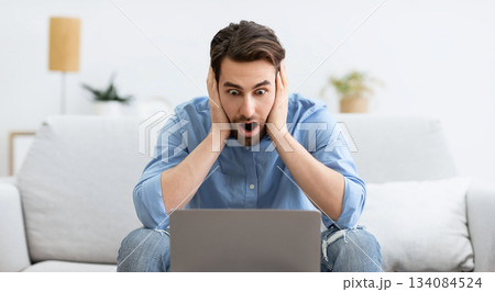Shocked Businessman At Laptop Computer Touching Head Having Problem Working Online Sitting On Couch At Home. Distance Work Issue And Internet Connection Problems 134084524