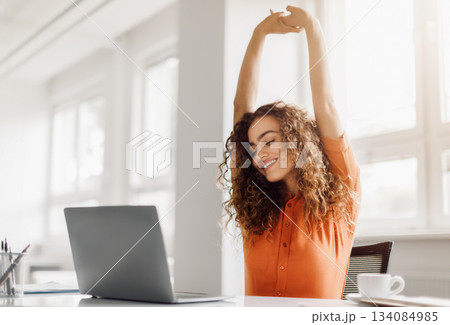 Joyful businesswoman taking a break to stretch, with closed eyes and a smile, at her workspace with a laptop, in a bright modern office setting, copy space Joyful businesswoman taking a break to stretch, with closed eyes and a smile, at her workspace with a laptop, in a bright modern office setting, copy space 134084985