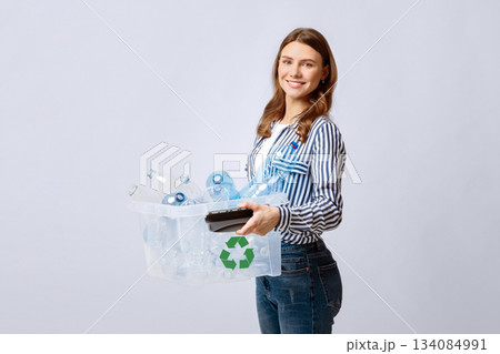 Recyclable Materials. Young Smiling Woman Holding Container With Empty Plastic Bottles For Recycling, Positive Eco-Volunteer Lady Enjoying Zero-Waste System, Standing Over Light Background, Free Space 134084991