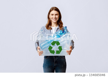 Waste Reuse. Cheerful Young Woman Carrying Container With Plastic Bottles For Recycling And Smiling At Camera, Happy Eco-Activist Sorting Garbage For Recycle, Standing On Grey Background 134085046