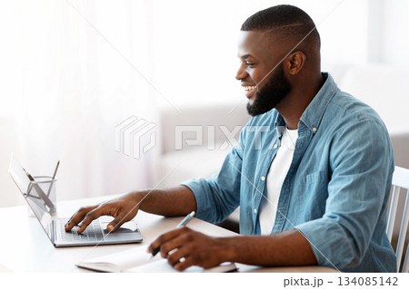 Online Education. Young Smiling Black Guy Study With Laptop At Home And Taking Notes, Handsome Millennial African American Man Watching Webinar And Noting Infornation From Computer, Copy Space 134085142