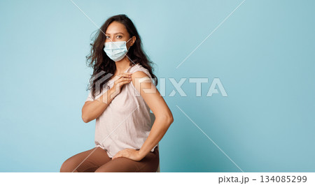 Covid-19 Vaccination. Vaccinated Lady Showing Arm After Coronavirus Antiviral Vaccine Injection Sitting Over Blue Background, Wearing Face Mask. Corona Virus Prevention. Panorama, Empty Space 134085299