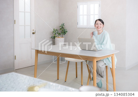 パソコンを使いながらコーヒーを飲む女性　広角の全身　カメラ目線 134085304