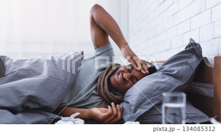 Ill African American Guy Having Severe Headache Suffering From Pain Touching Aching Head Lying In Bed At Home. Migraine During Influenza And Cold Concept. Selective Focus Ill African American Guy Having Severe Headache Suffering From Pain Touching Aching Head Lying In Bed At Home. Migraine During Influenza And Cold Concept. Selective Focus 134085312