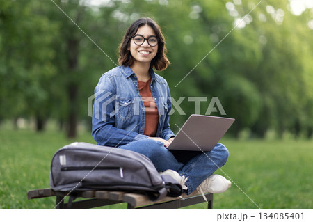 Portrait Of Happy Middle Eastern Female Student Sitting On Bench Outdoors With Laptop, Beautiful Young Arab Woman Using Computer In Park, Enjoying Online Education And Distance Learning, Copy Space Portrait Of Happy Middle Eastern Female Student Sitting On Bench Outdoors With Laptop, Beautiful Young Arab Woman Using Computer In Park, Enjoying Online Education And Distance Learning, Copy Space 134085401