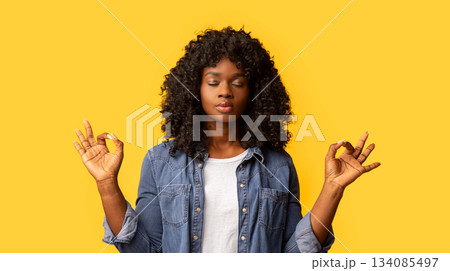 Staying calm and relaxed in urban atmosphere. Cute determined dark-skinned woman in casual outfit, closing eyes and raising hands in zen gesture, meditating or practicing yoga over yellow background Staying calm and relaxed in urban atmosphere. Cute determined dark-skinned woman in casual outfit, closing eyes and raising hands in zen gesture, meditating or practicing yoga over yellow background 134085497