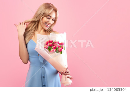 Cheerful millennial lady with bouquet of beautiful flowers on pink studio background. Pretty young blonde with bunch of tulips celebrating Woman's Day. Spring holiday concept Cheerful millennial lady with bouquet of beautiful flowers on pink studio background. Pretty young blonde with bunch of tulips celebrating Woman's Day. Spring holiday concept 134085504
