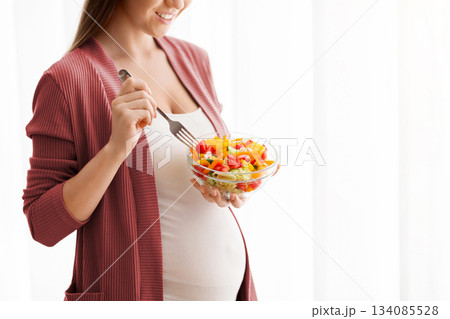 Pregnant Woman With Bowl Of Vegetable Salad Standing Near Window At Home, Unrecognizable Expectant Lady Eating Begetarian Lunch And Enjoying Healthy Nutrition During Pregnancy, Cropped, Copy Space Pregnant Woman With Bowl Of Vegetable Salad Standing Near Window At Home, Unrecognizable Expectant Lady Eating Begetarian Lunch And Enjoying Healthy Nutrition During Pregnancy, Cropped, Copy Space 134085528