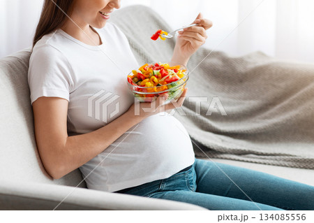 Vitamin Food. Happy Young Pregnant Woman Eating Vegetable Salad While Sitting On Couch At Home, Relaxing In Living Room And Enjoying Healthy Organic Nutrition During Pregnancy, Side View, Copy Space Vitamin Food. Happy Young Pregnant Woman Eating Vegetable Salad While Sitting On Couch At Home, Relaxing In Living Room And Enjoying Healthy Organic Nutrition During Pregnancy, Side View, Copy Space 134085556