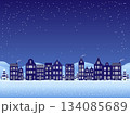 A winter night scene featuring a charming row of old-style houses softly illuminated against a deep blue sky, while delicate snowflakes sparkle in the night air.	 134085689