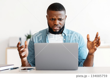 Deadline Stress. Annoyed black man sitting at workplace looking at laptop screen, african american freelancer guy suffering business problems while working online on computer at home office Deadline Stress. Annoyed black man sitting at workplace looking at laptop screen, african american freelancer guy suffering business problems while working online on computer at home office 134085759