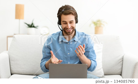 Businessman At Laptop Watching Educational Business Webinar Online Wearing Headset Sitting On Sofa Indoors. Distant Computer Work, Video Call And Internet Business Training Concept 134085760
