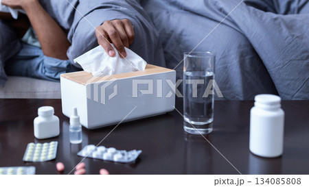 Ill African American Man Sneezing Having Sinusitis Lying On Sofa At Home. Sick Black Guy Blowing Runny Nose In Paper Handkerchief Suffering From Cold And Rhinitis Symptoms. Selective Focus 134085808