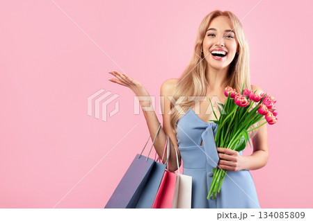 Happy young lady with shopping bags and bouquet of tulips buying gifts for spring holiday over pink studio background. Woman's Day sale, discount or promotion concept 134085809