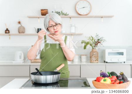 マイホームのキッチンで料理中に味見をするエプロン姿のシニア女性 マイホームのキッチンで料理中に味見をするエプロン姿のシニア女性 134086800