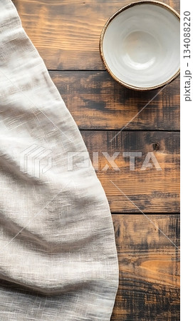 Light linen cloth and an empty ceramic bowl rest atop a rustic wooden table 134088220