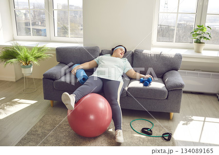 Tired exhausted overweight woman in sportswear lying on sofa at home Tired exhausted overweight woman in sportswear lying on sofa at home 134089165