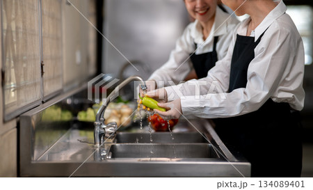Asian female chefs is washing or cleaning a green pepper with tab water in restaurant's kitchen sink Asian female chefs is washing or cleaning a green pepper with tab water in restaurant's kitchen sink 134089401