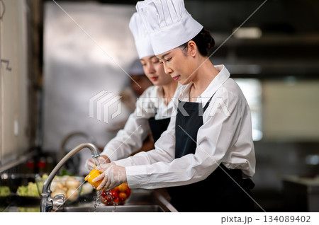Asian female chefs is washing or cleaning a bell pepper with tab water in restaurant's kitchen sink Asian female chefs is washing or cleaning a bell pepper with tab water in restaurant's kitchen sink 134089402
