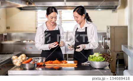 Female chef teaching how to cut a tomato to her student or an assistant at kitchen cooking counter. Female chef teaching how to cut a tomato to her student or an assistant at kitchen cooking counter. 134089418