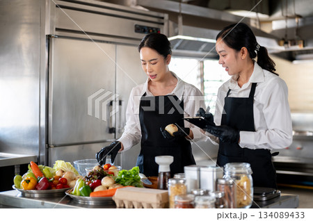 Student or assistant note down while female chef teaching at kitchen counter with food ingredients. 134089433