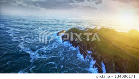 White lighthouse is standing on coastal cliff in flat design with sunlight and crashing waves 134090171