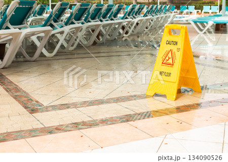 Warning sign caution wet floor among pool deck chairs near the hotel swimming pool 134090526