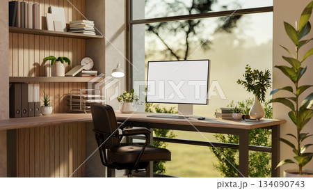Blank screen computer on a wooden table and armchair near glass wall with nature view outside. 134090743