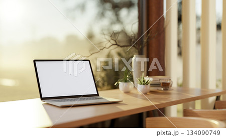 White screen laptop and a coffee cup on wooden counter in a glass wall cafe with nature view outside White screen laptop and a coffee cup on wooden counter in a glass wall cafe with nature view outside 134090749