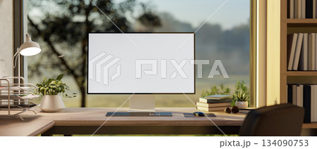 A white screen computer and lamp on wooden table under a glass window with green nature view outside A white screen computer and lamp on wooden table under a glass window with green nature view outside 134090753