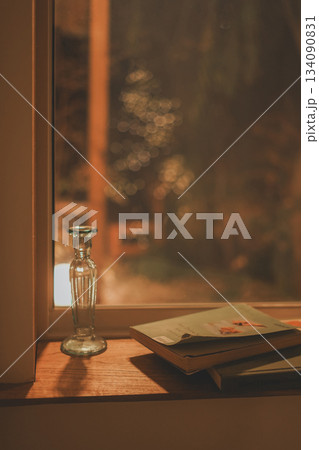 Books and vintage glass vases on warm indoor wooden windowsills 134090831